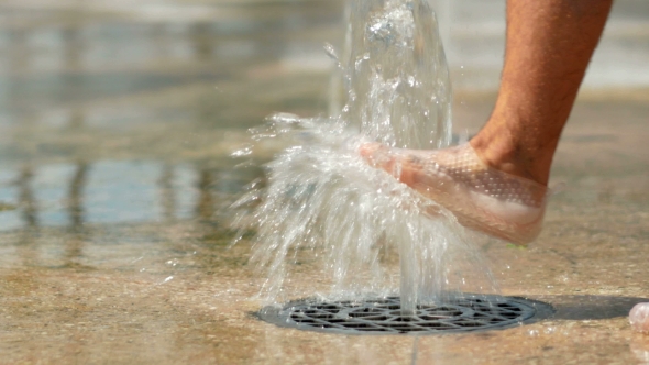 Water Pouring Out Of The Ground. Man's Foot Plays With Water. The Flow Of Water Falls To The Ground