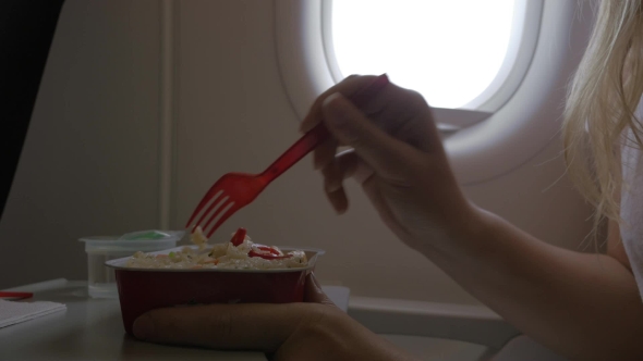 Clip Of Woman Eating Airplane Dinner Rise With Vegetables By Plastic Fork Against Window alt