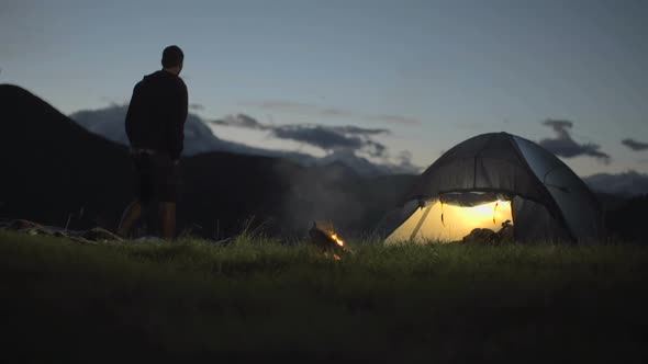 Young Man Walk in and Warming with Camp Fire in Nature Mountain Outdoor Camping Scene at Night alt