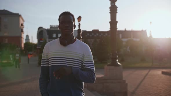A Young Black Student with Headphones Walks Through the City Centre at Sunset