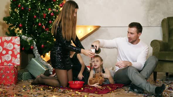 Happy Family of Four Sitting By the Christmas Tree and Eating Chocolate Cookies alt
