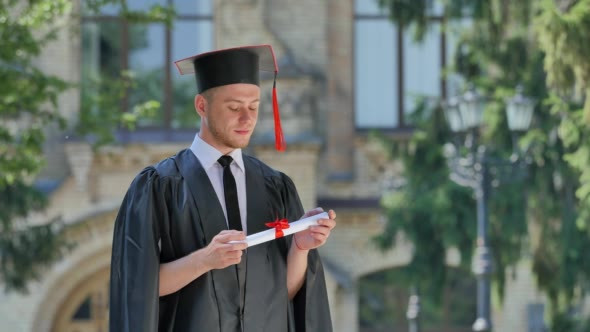 Graduand in Mantle Thinking Holding His Diploma alt
