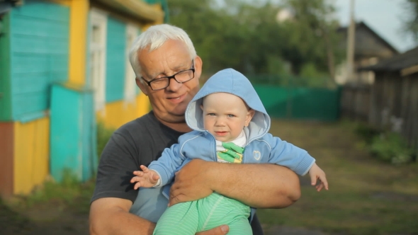 Grandfather Holding His Grandson In His Arms. Beautiful Baby Smiling