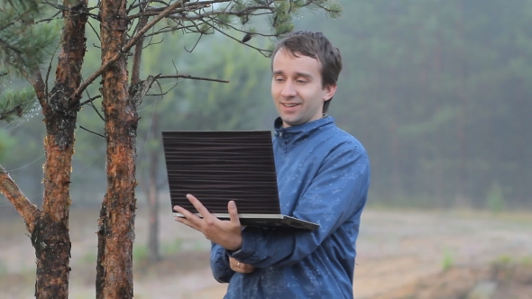 A Man Makes a Video Call On a Laptop Near a Tree In The Forest. Early Morning
