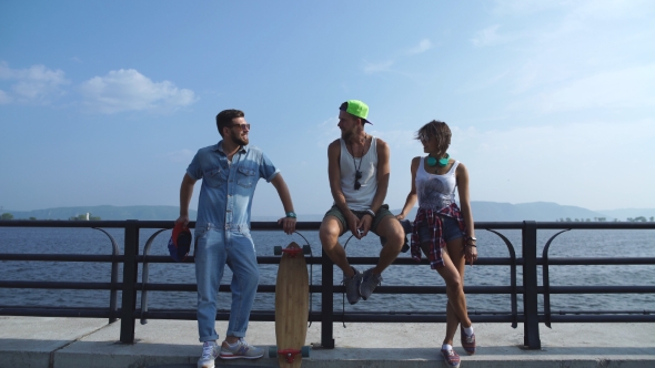 Three Young Friends With Skateboards Talking In The Background Of The River