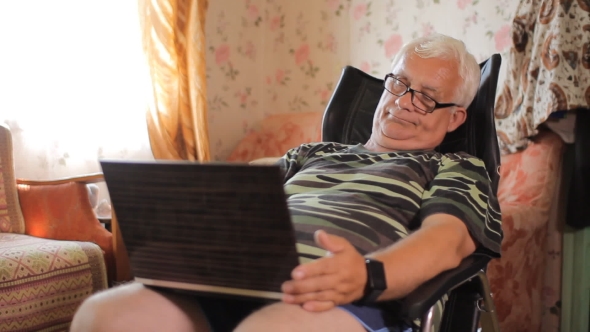 Senior Man Sitting With a Laptop In a Leather Chair At Home. Man Relaxing With a Computer