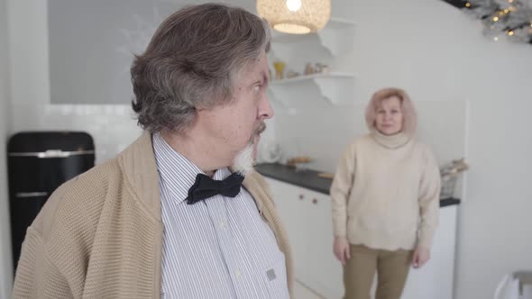 Annoyed Senior Man Looking Back at Blurred Woman Gesturing at the Background and Shaking Head alt