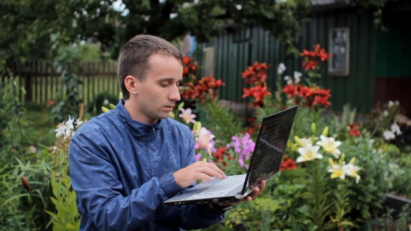 Young Man Working At a Laptop Near Beds Of Flowers