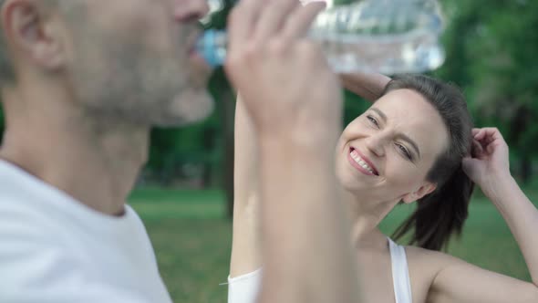 Beautiful Smiling Woman Adjusting Ponytail As Blurred Man Drinking Refreshing Water at Front alt