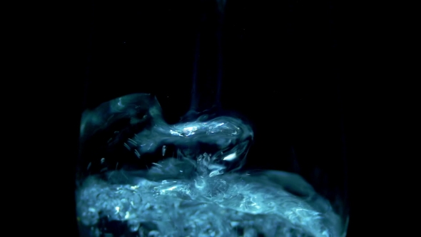 Water Is Poured Into a Transparent Glass On The Black Background. alt