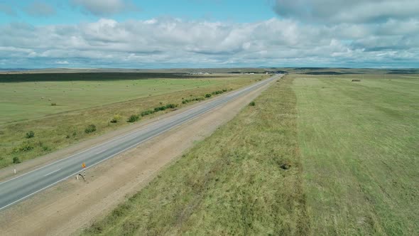 Aerial View of a Lorry Drives on an Intercity Road Between Green Fields Against Blue Sky with Clouds alt