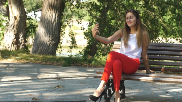 Beautiful Young Woman On a Park Bench Taking a Selfie alt