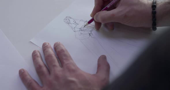 Top View of Male Designer's Hand Draws a Wedding Dress Sketch on a Desk alt