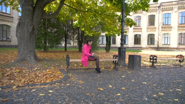 Young Girl In Pink Coat With Laptop On Bench In University Park
