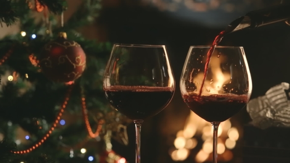 Pour The Wine Into The Glasses On The Background Of The Christmas Tree And Fireplace
