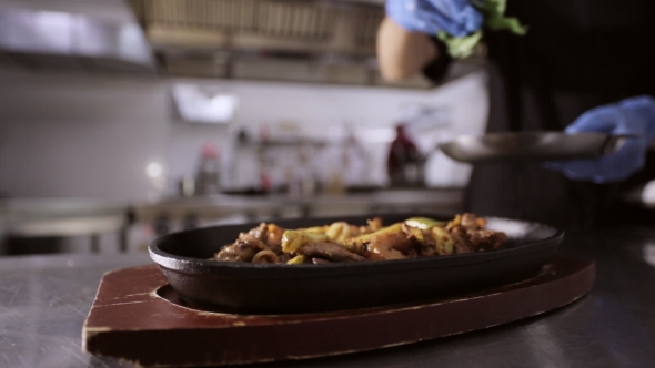 Chef Adding Herbs to Pan With Vegetables and Meat on Wooden Stand alt