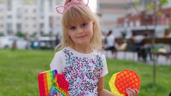 Stylish Children Girl Squeezing Presses Antistress Push Pop It Popular Toy on Playground Bench alt