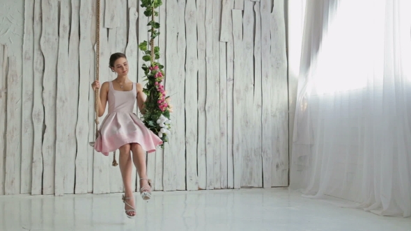 Pretty Woman With Make-up And Hairstyle On a Swing Decorated With Flowers. alt