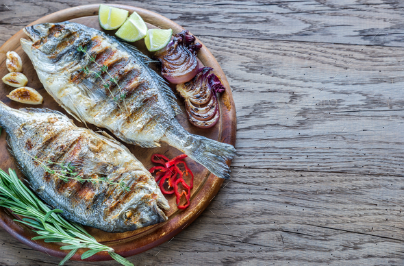 Three Gilt-head Bream On A Wooden Board With Limes And Herbs