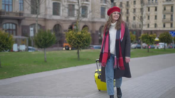 Wide Shot Portrait of Happy Smiling Young Woman Tourist Walking on City Street with Yellow Travel alt
