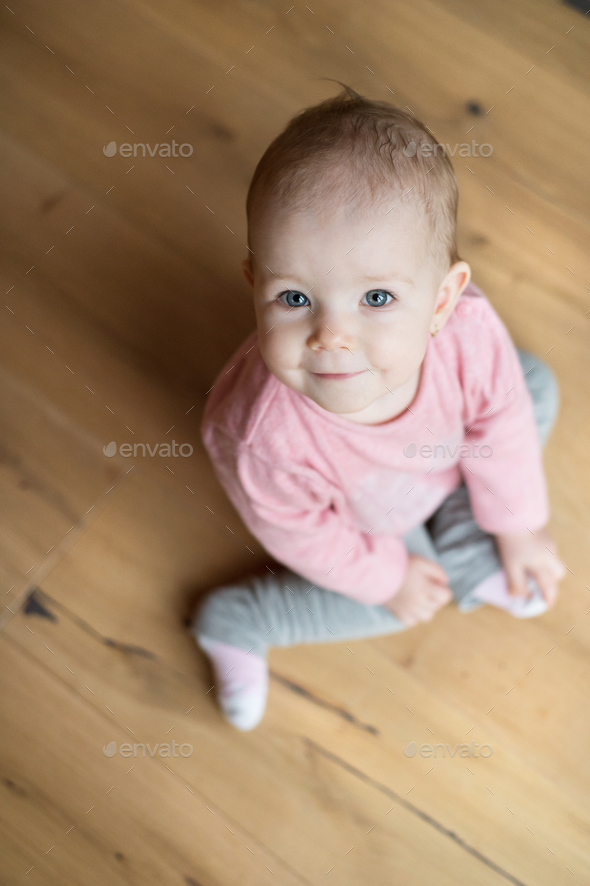 Cute little girl at home sitting on wooden floor, smiling Stock Photo ...