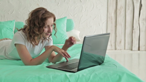 Curly Woman Lying On The Bed And Using Laptop