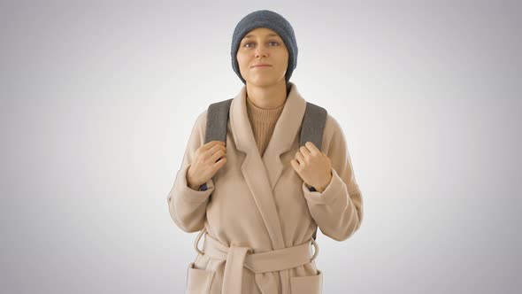 Young Woman Wearing Coat and Backpack Walking on Gradient Background. alt