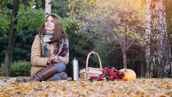 Young Woman Sitting On Picnic Drinking Hot Tea From a Thermos In Autumn Park. Girl Sitting On The