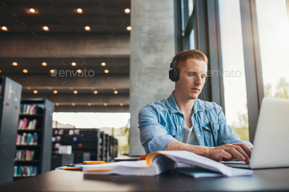 Male student working on laptop at public library - Stock Photo - Images