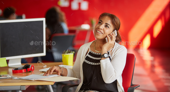 Confident female designer talking on a mobile phone in red creative office space - Stock Photo - Images