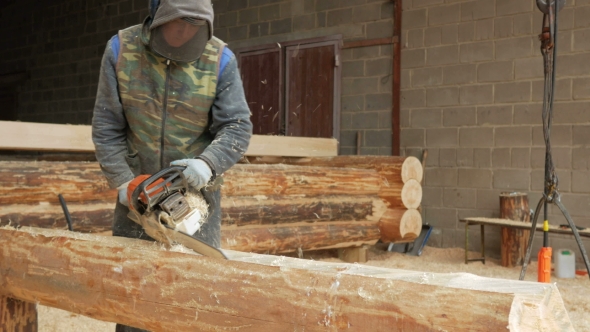 Man Cuts Wood Chainsaw For Future Home. Protective Face Mask On The Face Of The Builder