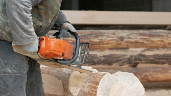 Construction Worker Cuts Wood Chainsaw For Future Home. Protective Mask And Headphones On The Head