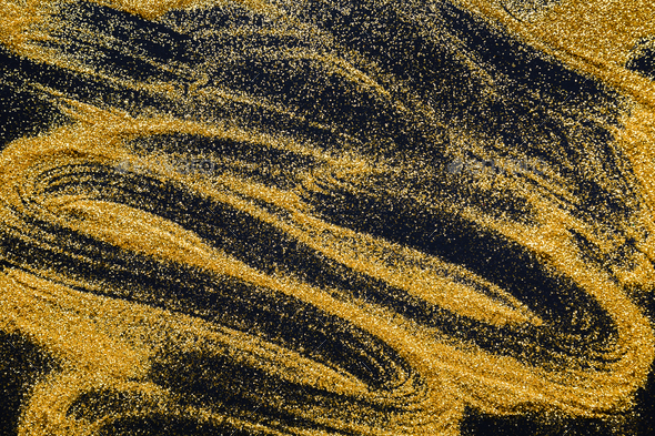 Sand painting. Golden glitter spread on black, abstract background.