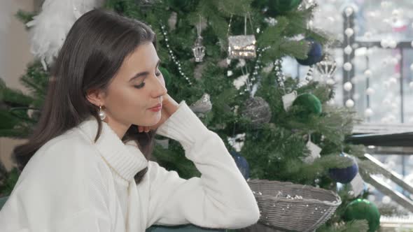 Gorgeous Woman Smiling to the Camera Sitting Near Christmas Tree at Home alt