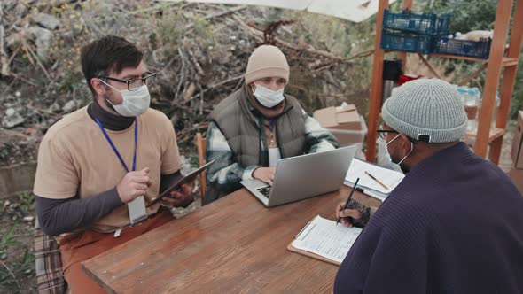 Social Workers in Face Masks Talking to Refugees under Tent alt