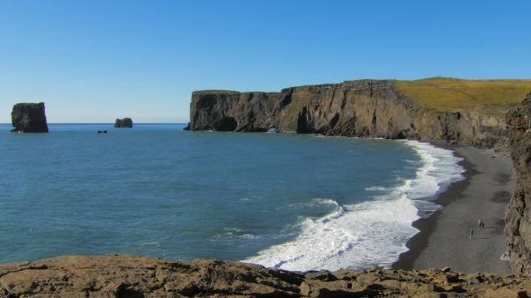 Cape Dyrholaey And Black Sand Beach With Strolling Tourists And Blue Waves