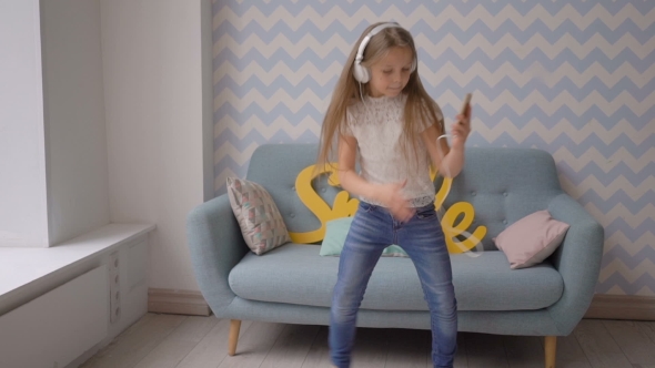Happy Child With Headphones And Smartphone Dancing And Listening To Music At Home