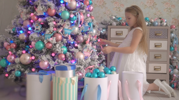 Little Girl In White Dress With Gifts Near Decorated New Year Tree