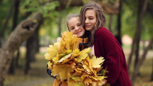 Two Sisters Hug, With a Bunch Of Leaves In The Park.