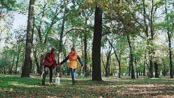 Two Young Women Running Hand In Hand, And Dog Fox Terrier. Jogging In The Autumn Forest. Falling