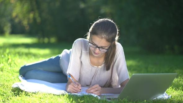 College Student Lying Down On The Grass And Working On Laptop