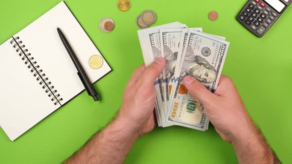 Young successful man's hands are counting many hundred dollar plans budget on green background