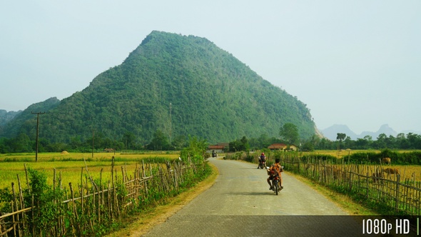 Remote Countryside Road in Southeast Asia with Motorcycle Traffic Rice Fields and Mountains alt