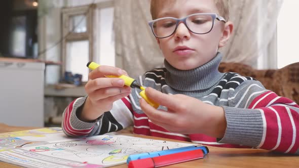 A Little Boy Paints a Coloring with Crayons and Felttip Pens on a Wooden Table at Home