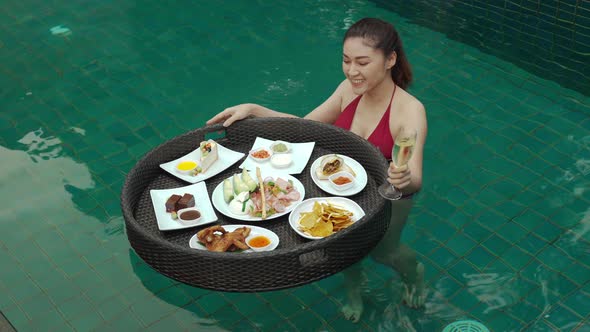 cheerful young woman enjoying with floating food and champagne glass in swimming pool