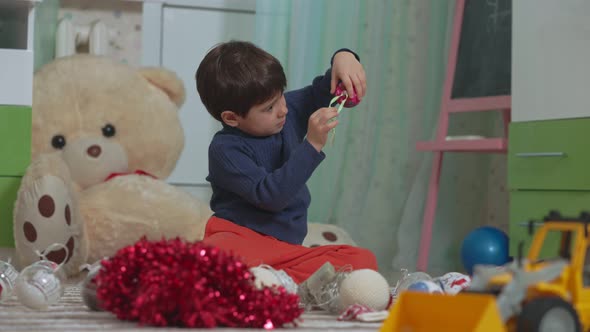 Little Baby Boy Chooses Christmas Tree Toys on the Floor of His Children's Room Against the alt