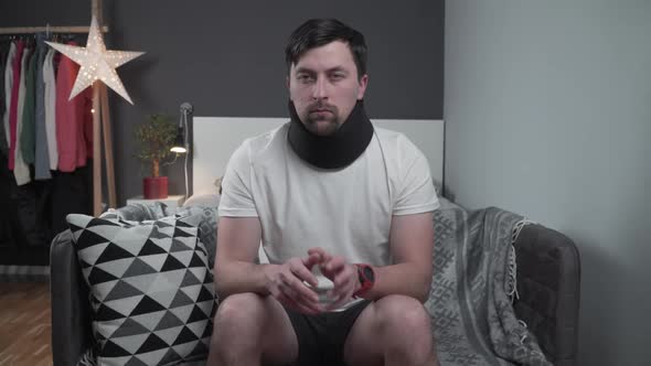 Man in Foam Collar After an Accident Suddenly Felt Sharp Pain in His Neck on Couch alt