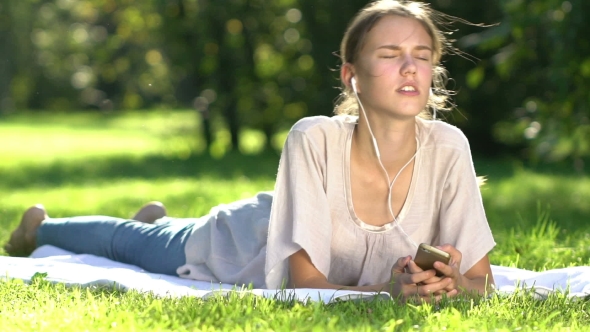 Young Woman Listening To Music And Using Smartphone In The Park