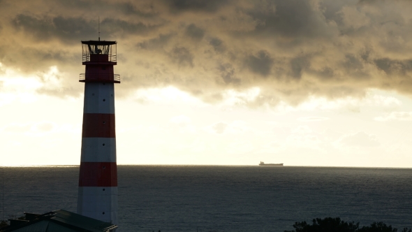 Lighthouse On The Sea Under Stormy Clouds And With The Ship In The Background alt