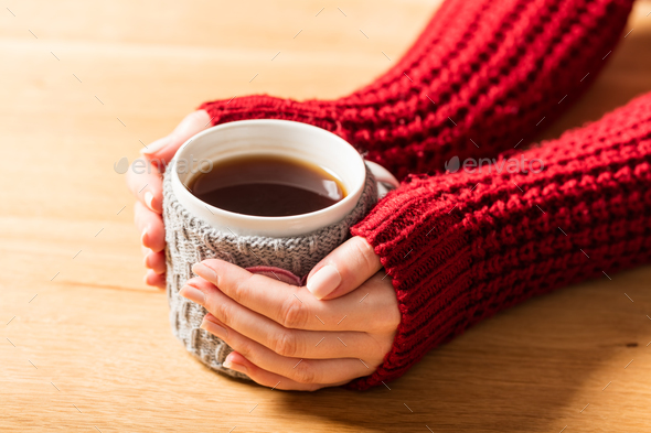 Hot mug of tea warming woman\'s hands in retro jumper.